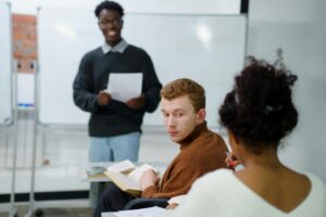 Instructor holding paper and students at desks. Image source: Pexels