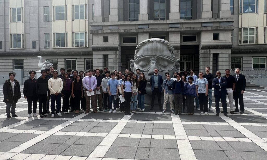 Students and professor standing outside of a courthouse with statue of a head in the background