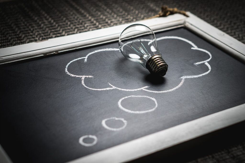 Lightbulb sitting on a thought bubble drawn in chalk on a chalkboard