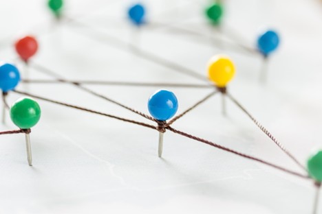 Colored pushpins connected by string on a map or board, representing a network.