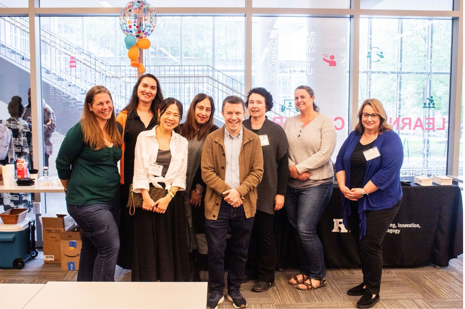 Members of the Course Design Institute team pose together in front of a window with celebratory balloons marking the institute's one-year anniversary.
