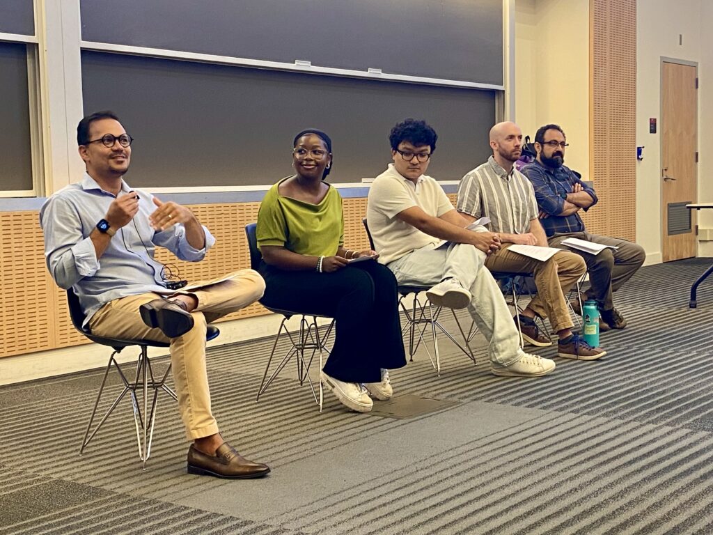 Five people sitting in chairs in the front of an auditorium for a panel discussion