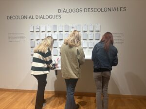 Three students facing away from the photograph, completing an activity at the "Decolonial Dialogues" exhibit.