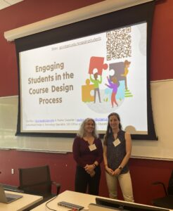 Two female facilitators stand in front of a projected PPT slideshow entitled "Engaging Students in the Course Design Process".