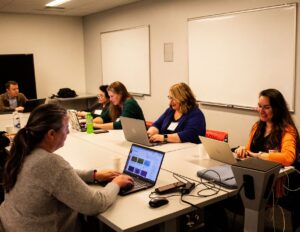A small group of Course Design Institute participants sit around a conference table, collaborating and working on their laptops.
