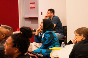 This photo shows several Course Design Institute participants sitting during a presentation. The focus of the image is a participant, female, who is smiling.