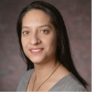 Headshot of a woman in a gray shirt, smiling in front of a brownish-gray background.