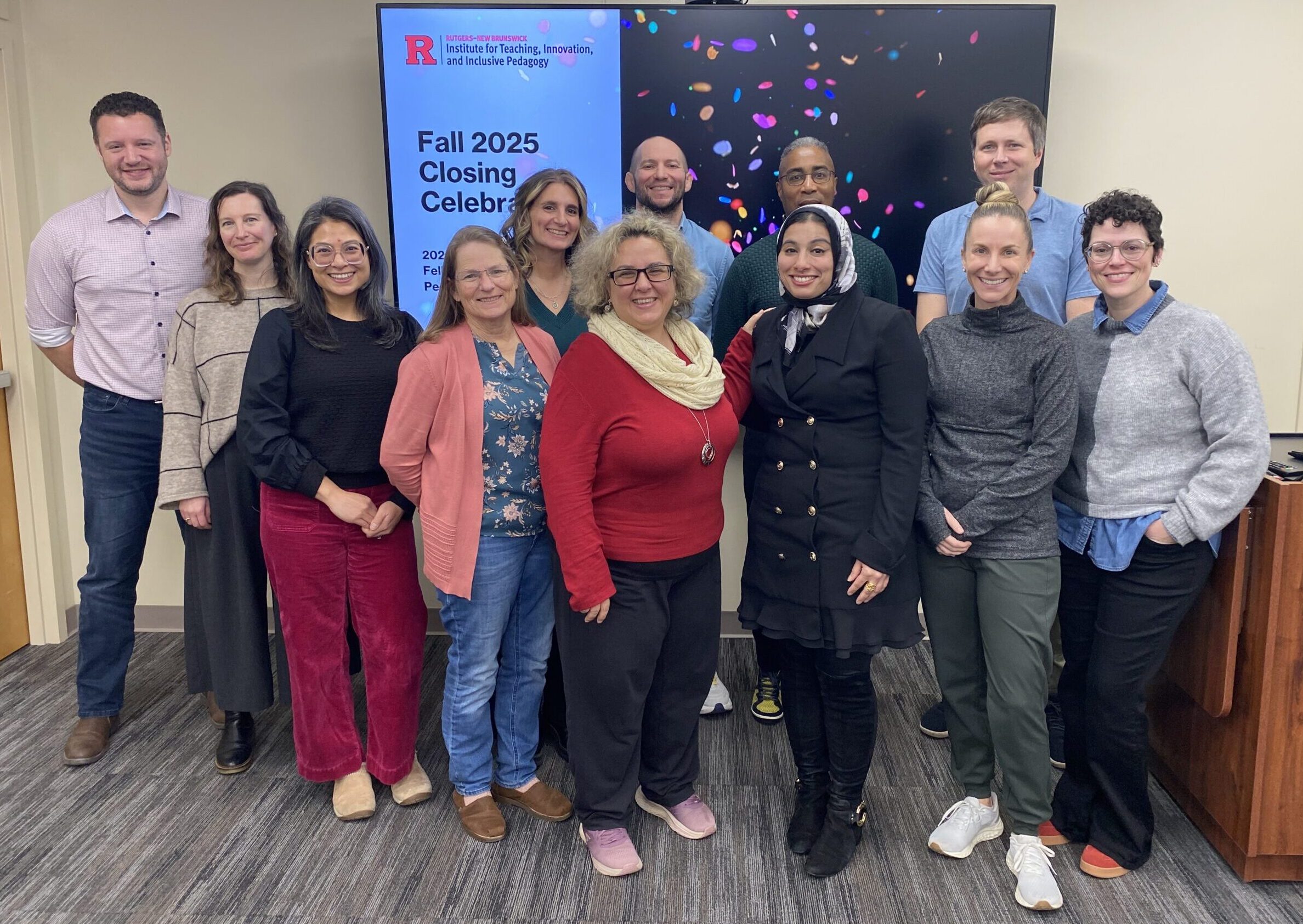 Group photo taken indoors at a Rutgers–New Brunswick event. Twelve people stand in two rows in front of a large display screen. The screen shows Rutgers–New Brunswick Institute for Teaching, Innovation, and Inclusive Pedagogy branding and the text “Fall 2025 Closing Celebration,” with a colorful confetti graphic. The participants are posing for a commemorative photograph in a classroom or meeting space with light-colored walls, carpeted flooring, and a lectern visible on the right.
