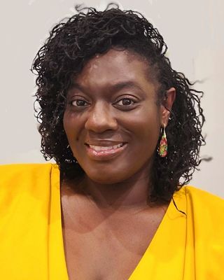 Headshot of a woman in a yellow shirt, smiling in front of a light gray background.