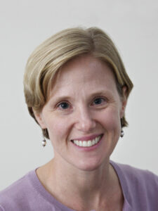 A headshot of a woman with short blond hair and a pink shirt, smiling.