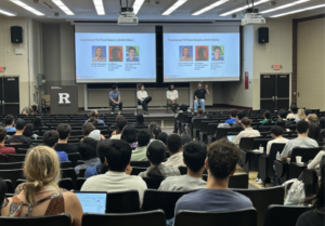 New TAs sit in the audience in a large lecture room, listening to a panel session.